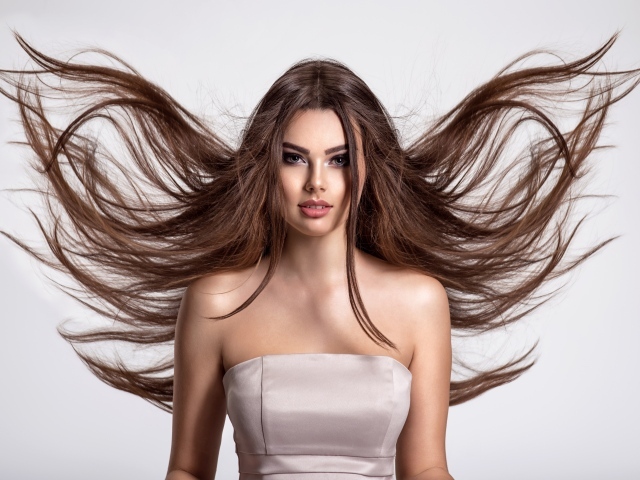 Ветер развивает волосы красивой девушке шатенке на сером фоне