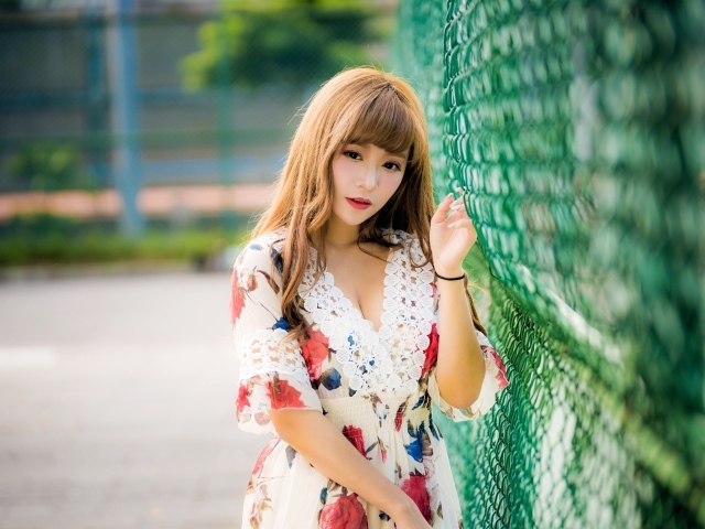 Молодая азиатка в платье у зеленой сетке 