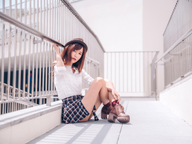 Молодая азиатка в короткой юбке сидит у перил 