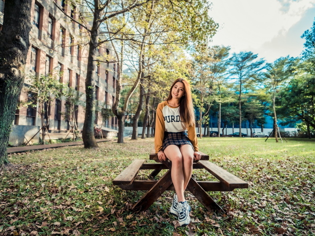 Молодая азиатка сидит на деревянном столе в парке 