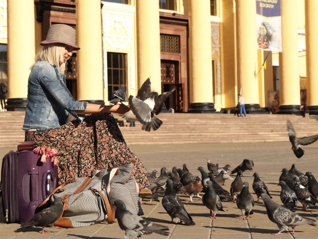 Молодая девушка кормит голубей на вокзале