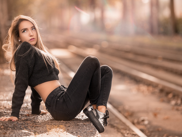 Молодая девушка в джинсах сидит у железной дороги 
