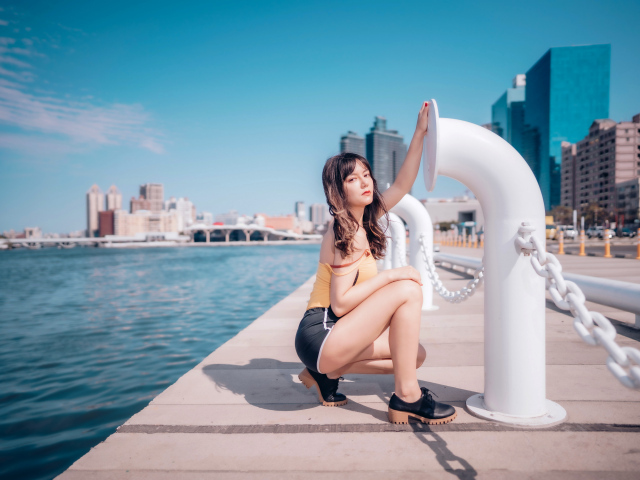 Молодая девушка в шортах сидит на пирсе