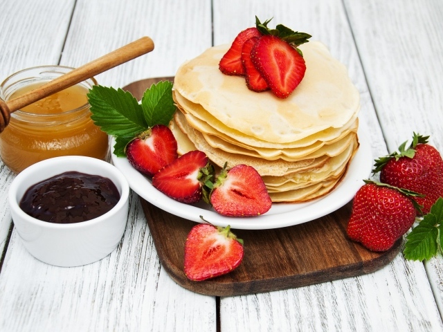 Блины с клубникой на столе с медом и джемом на праздник Масленица 2020