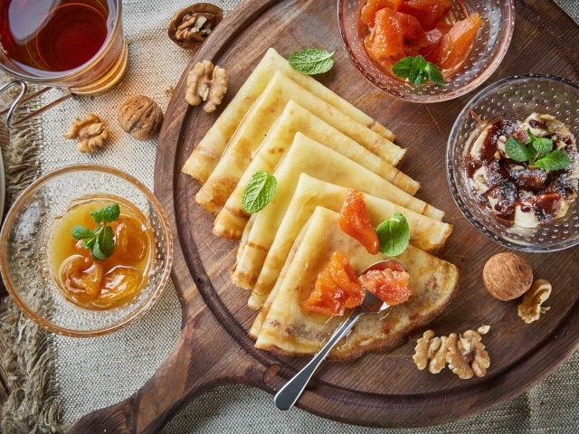 Тонкие блины с орехами и джемом на столе на Масленицу