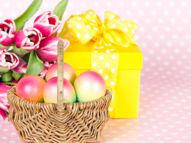 Корзина с пасхальными яйцами на столе с подарком и букетом тюльпанов 
