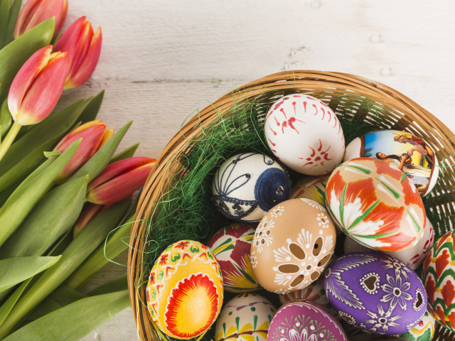 Разноцветные крашеные яйца в корзине с букетом тюльпанов на Пасху