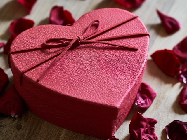 Большая красная коробка в форме сердца на столе с лепестками роз