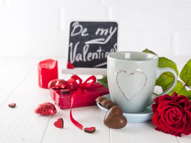 Белая чашка с конфетами и красной розой на столе в подарок на 14 февраля