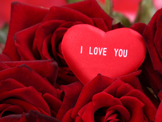 Маленькое сердце лежит на букете красных роз 