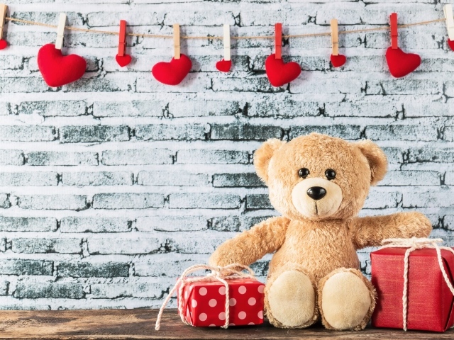 Медвежонок Тедди с подарками на фоне стены с сердечками