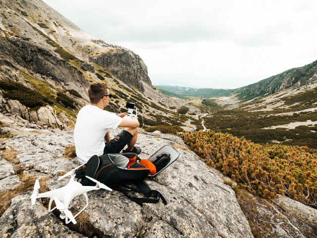 Парень с квадрокоптером сидит на камне в горах 