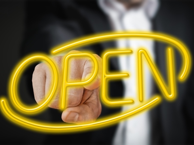 Мужчина трогает пальцем желтую  неоновую  надпись Open 