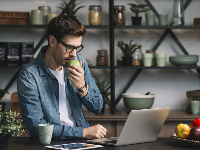 Мужчина с ноутбуком ест яблоко в кафе 