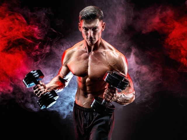 Мускулистый мужчина с гантелями в руках на черном фоне с дымом