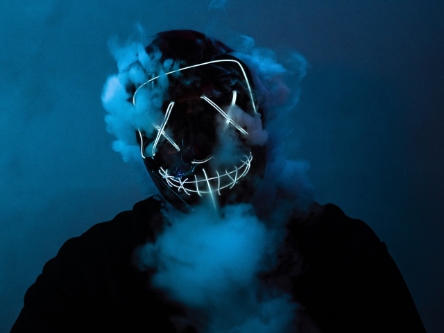 Дым идет из под неоновой маски анонимуса на лице у парня