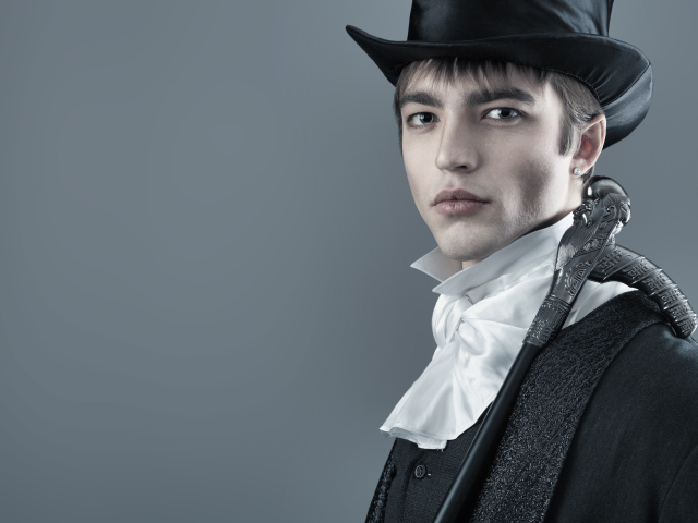 Красивый молодой человек в черном цилиндре и фраке на сером фоне