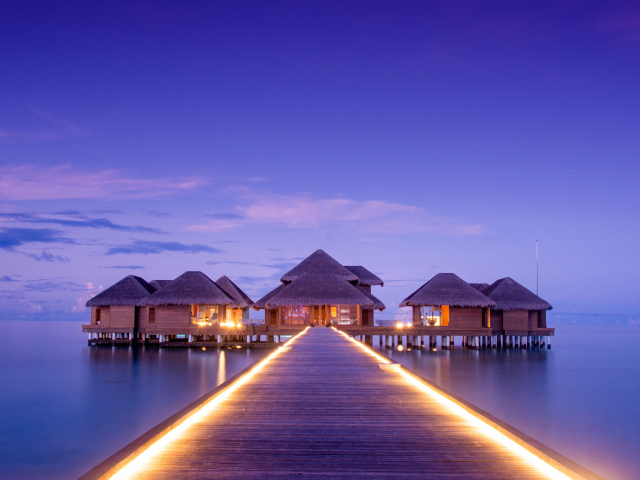 Мост с подсветкой идет к домам на сваях в океане