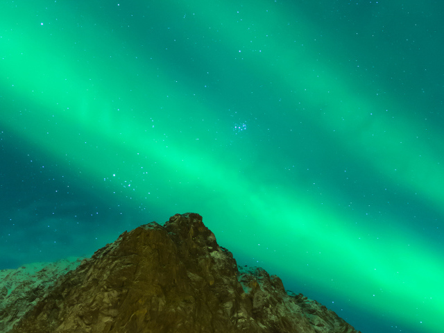 Зеленое северное сияние над верхушкой скалы в небе 