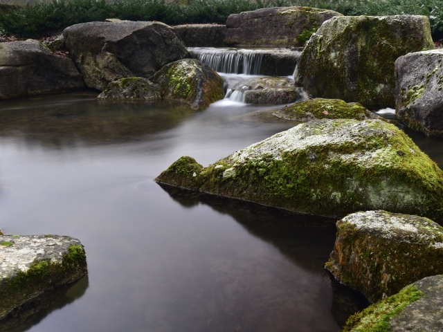 Вода стекает по камням в пруд с большими покрытыми мхом камнями