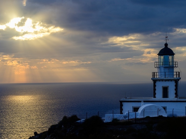 Белый маяк на берегу в лучах солнца у моря 
