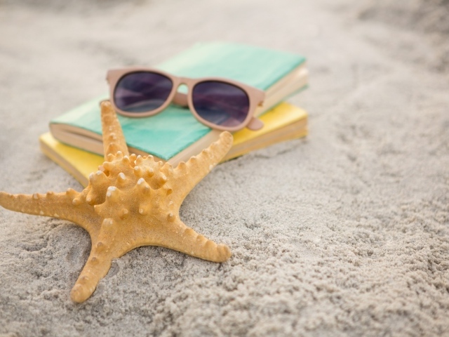 Книги, очки и морская звезда на белом песке 