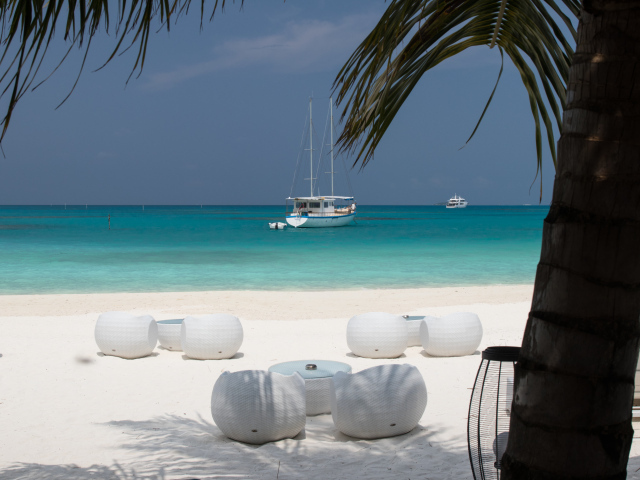 Белые кресла и столики на белом песке на пляже у голубой воды