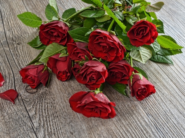 Красивый букет алых роз с зелеными листьями на деревянном столе