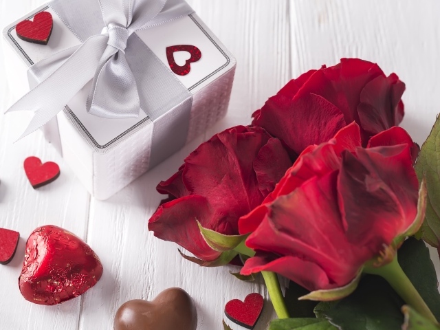 Букет красных роз на столе с конфетами и подарком