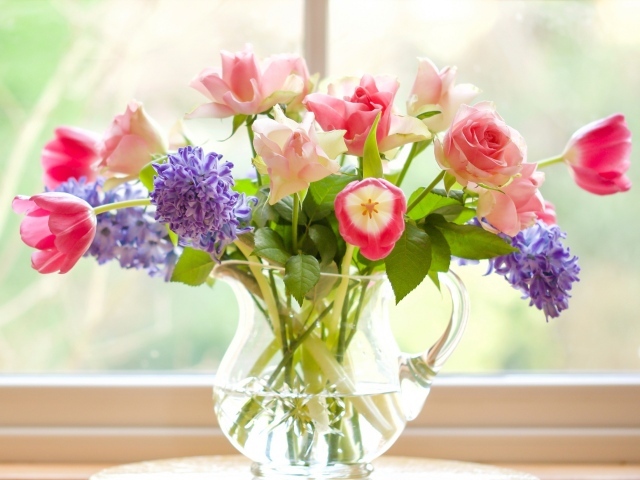 Букет роз, тюльпанов и гиацинтов в стеклянной вазе у окна