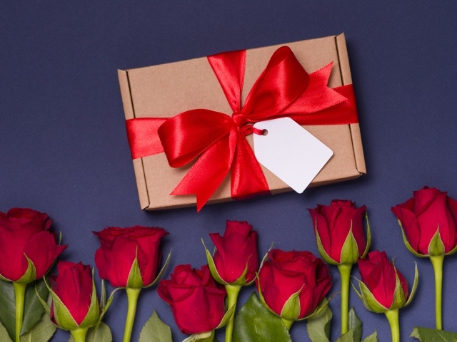 Подарок с красным бантом на столе с розами