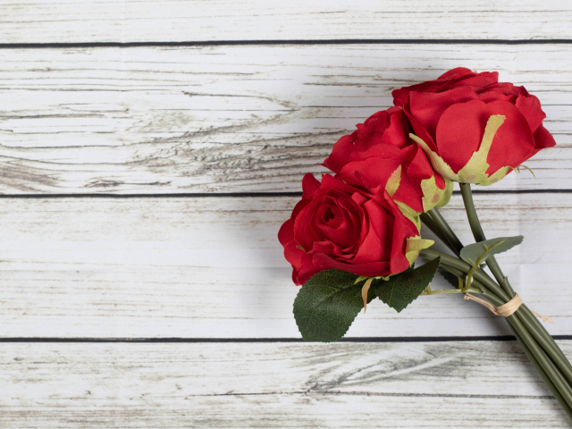 Три искусственные красные розы на деревянном фоне