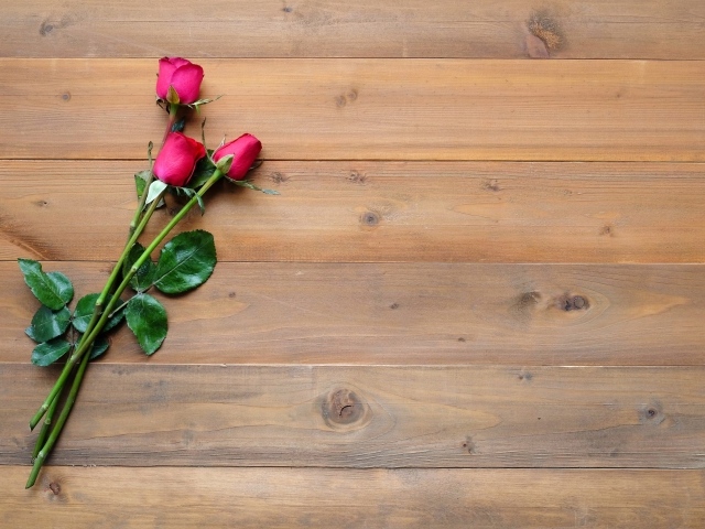 Три красные розы лежат на деревянном столе 