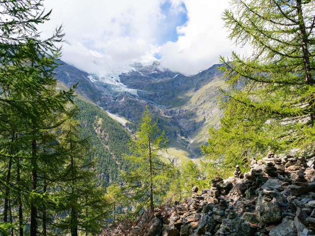 Высокие покрытые хвойным лесом горы под облачным небом 