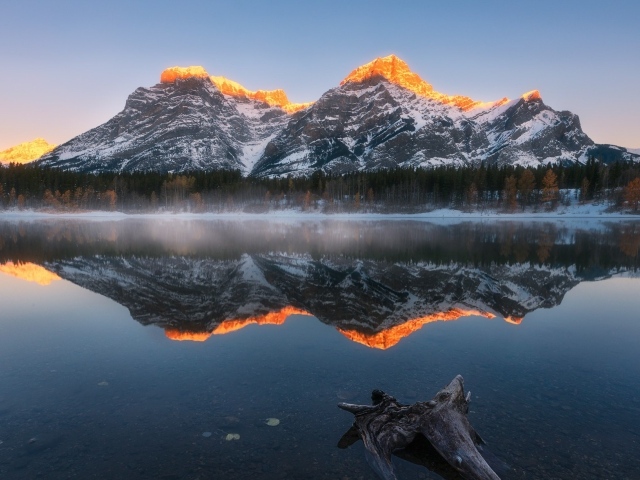 Вершины гор в лучах солнца отражаются в чистой воде озера