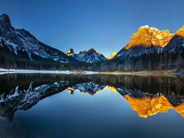 Вершины гор в лучах солнца отражаются в озере