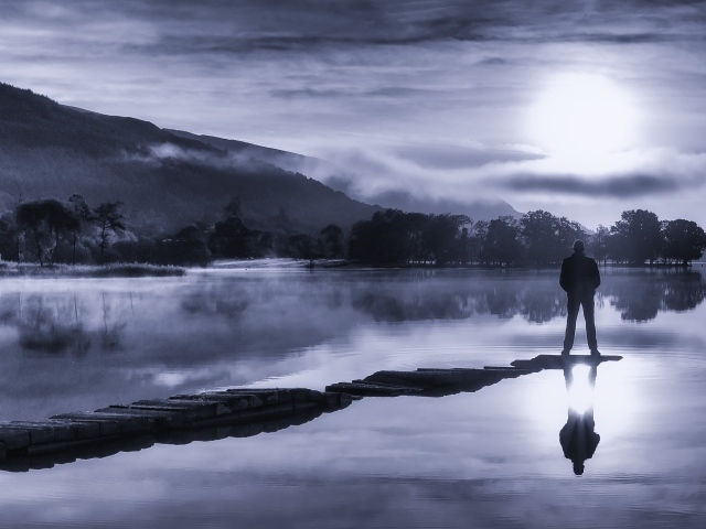 Мужчина стоит на мосту у озера ночью при свете луны