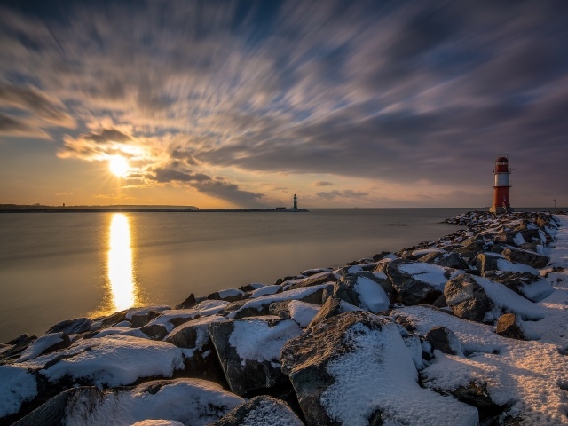 Заснеженные камни на берегу моря с маяком на закате