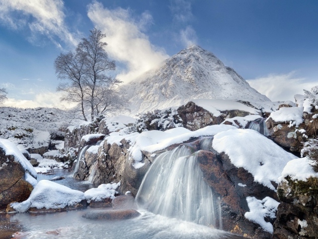 Водопад стекает с камней на фоне заснеженной горы