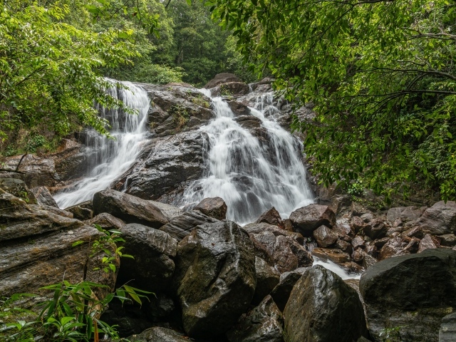 Водопад стекает по большим мокрым камням в лесу 
