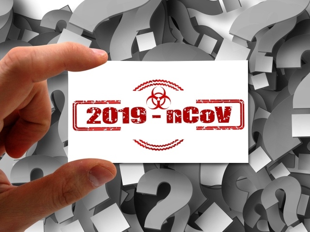 Табличка коронавирус covid-19 в руке на фоне знаков вопроса