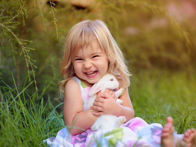 Довольная маленькая девочка обнимает белого кролика на траве 