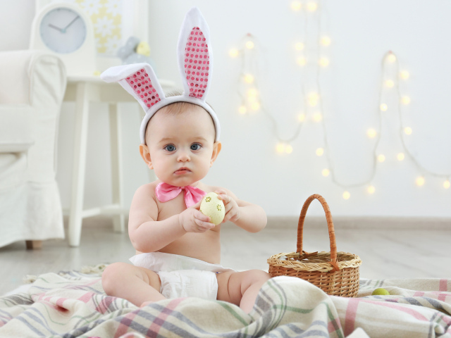 Милый ребенок с ушками на голове сидит пасхальными яйцами