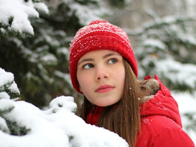 Милая девочка в красной шапке у заснеженной ели