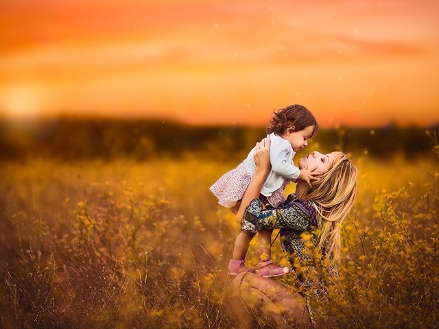 Девушка держит маленькую девочку на руках в поле на закате