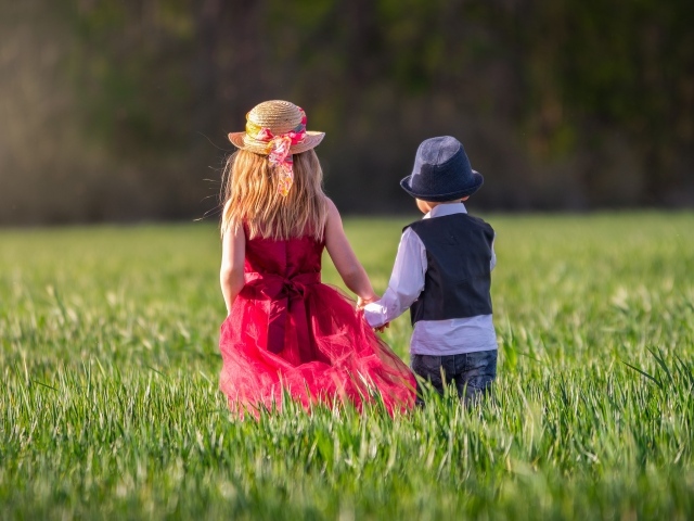 Маленькие мальчик и девочка идут по зеленому полю
