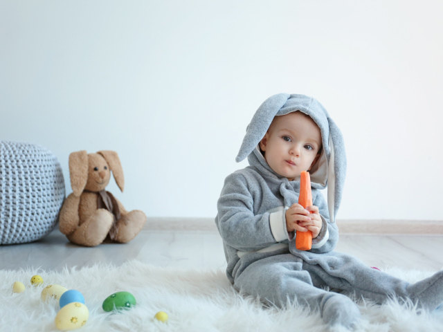 Маленький мальчик в костюме зайчика грызет морковь