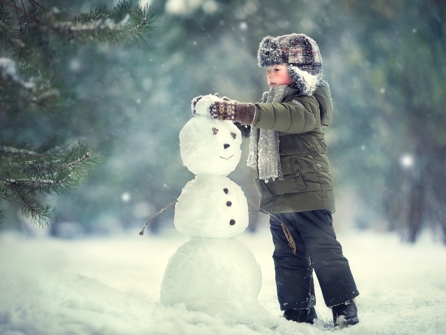 Маленький мальчик лепит снеговика зимой