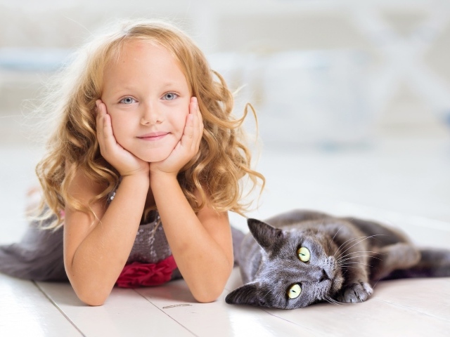 Маленькая милая голубоглазая девочка лежит на полу с котом