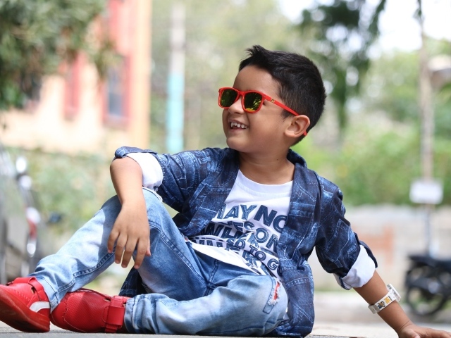 Маленький модный мальчик сидит на асфальте